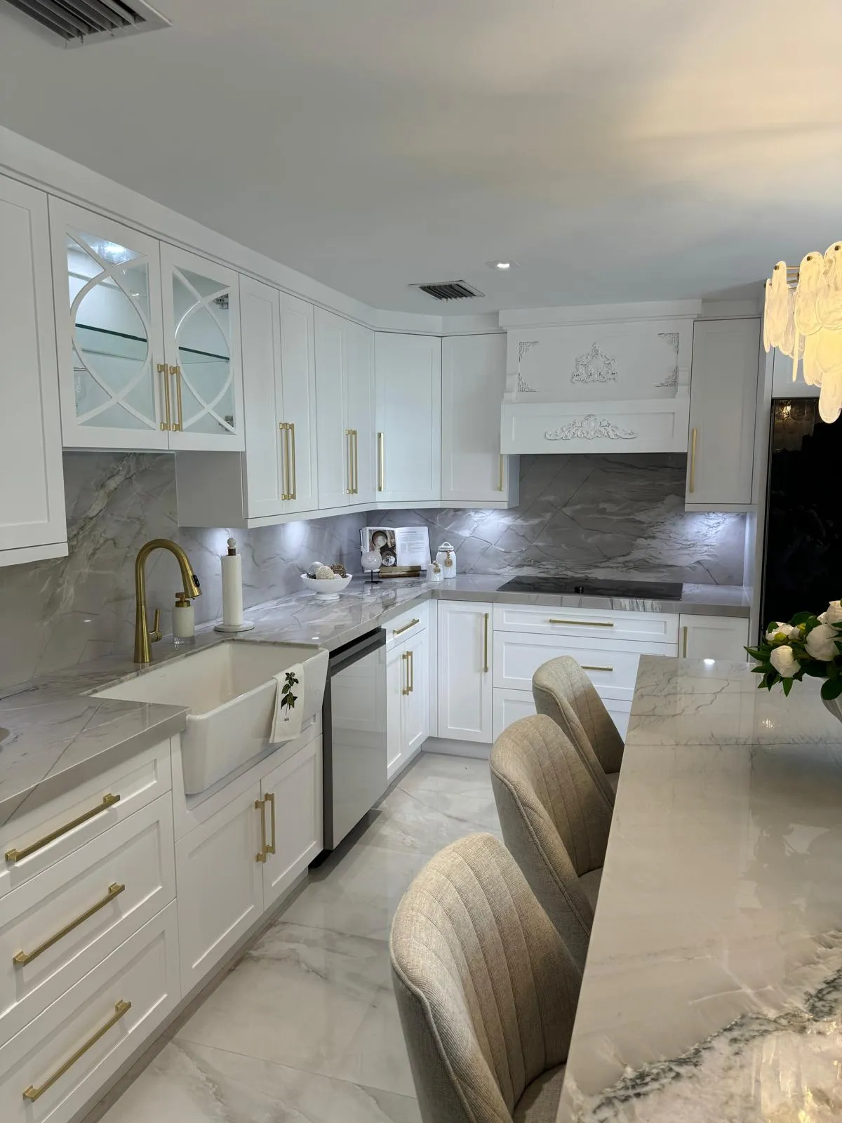White kitchen with farmhouse sink, gold fixtures and a carved range hood
